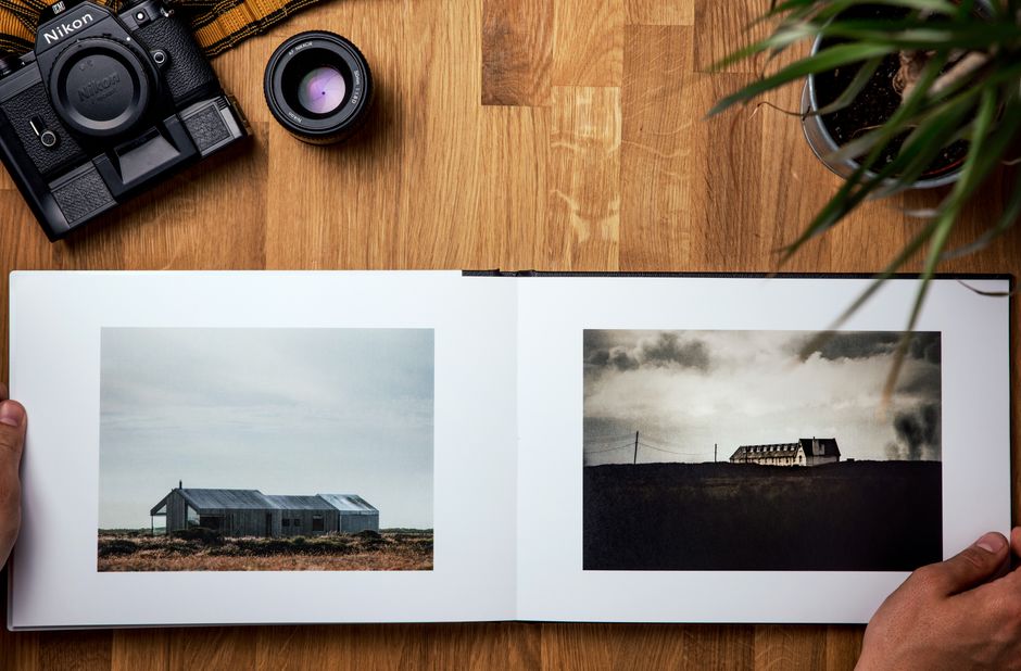 Overhead view of pictures in opened photo album composing with pot plant and modern photo camera next to lens on wooden table in bright room